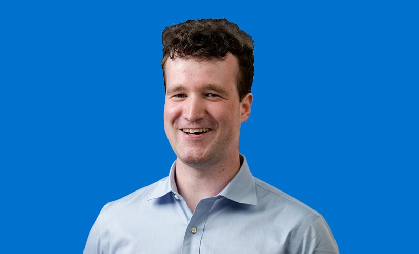 Image of male graduate with blue background behind him 