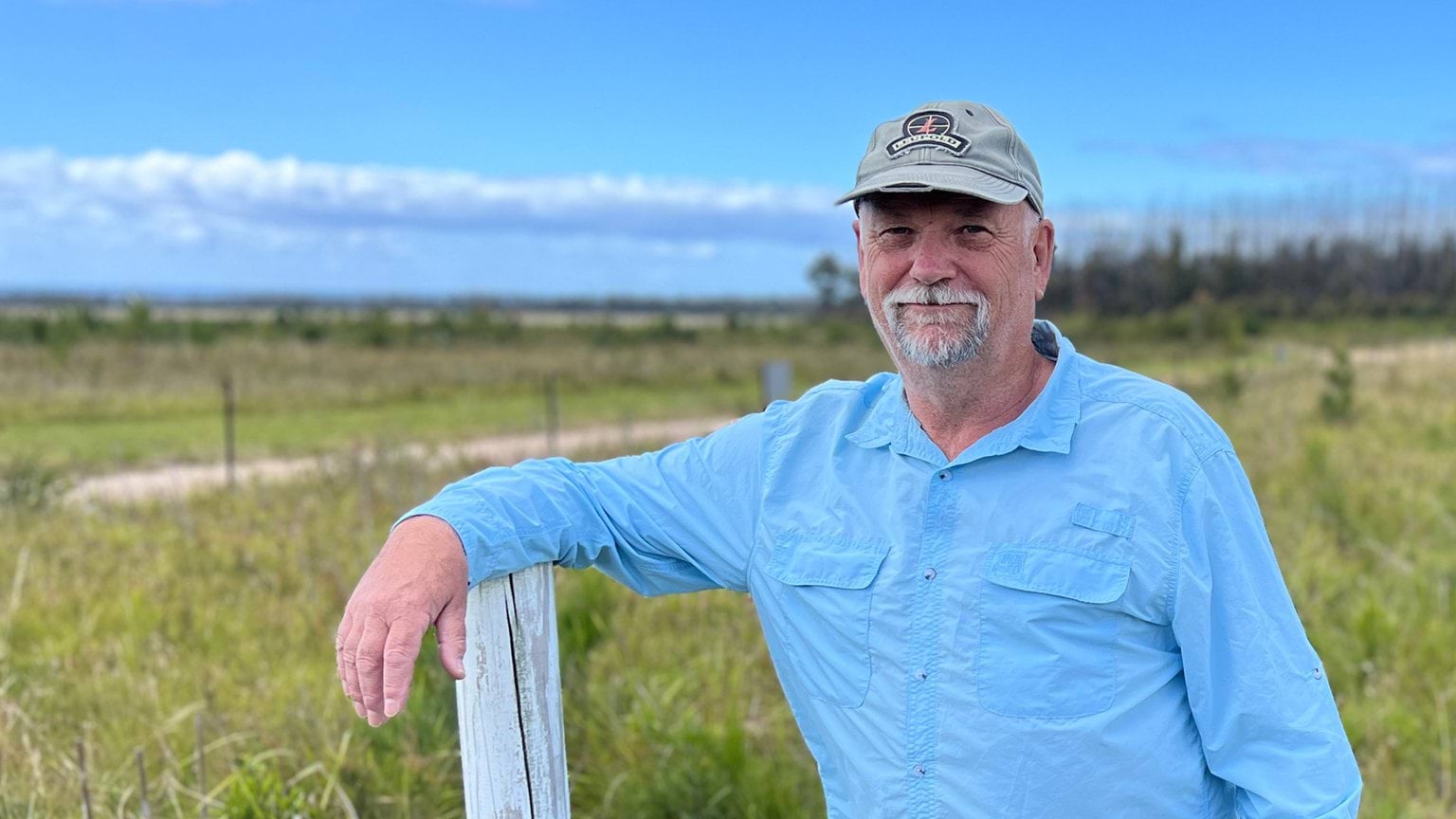 Mallacoota Gun Club, Treasurer, Dave Whittle wearing a blue shirt and leaning on a fence post in an outdoor field setting