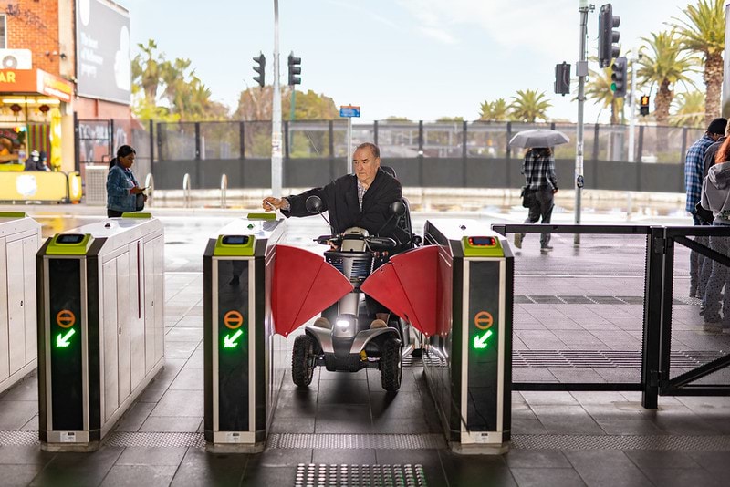 Person using a mobility scooter tapping their myki at the accessible train station gates