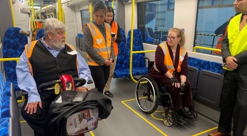 Photo of a group of people on the X’Trapolis 2.0 train mock-up. One person is using a manual wheelchair, and another is using a mobility scooter.