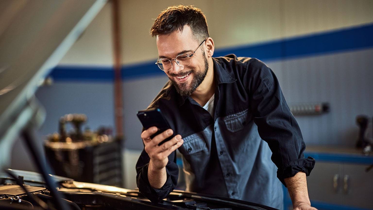 person working on car engine looking at a mobile device