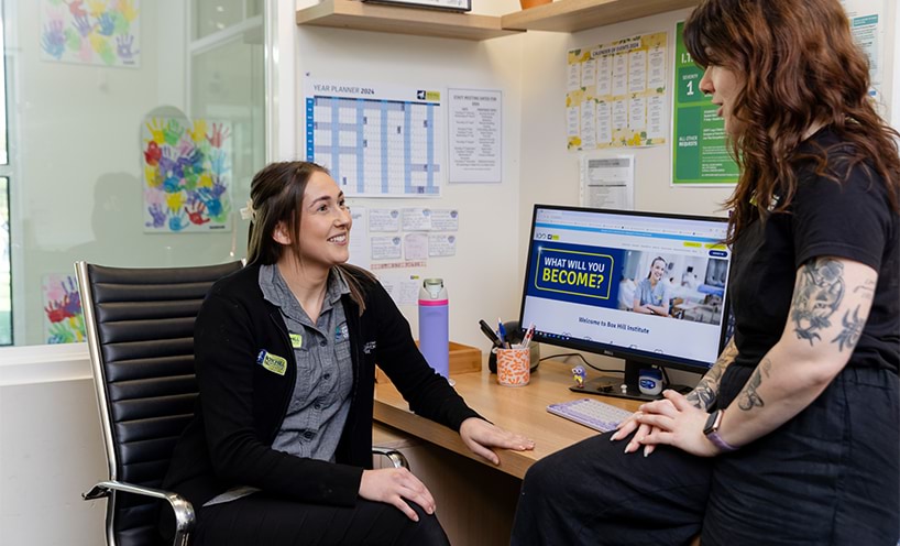 Two women sitting and chatting at a desk.