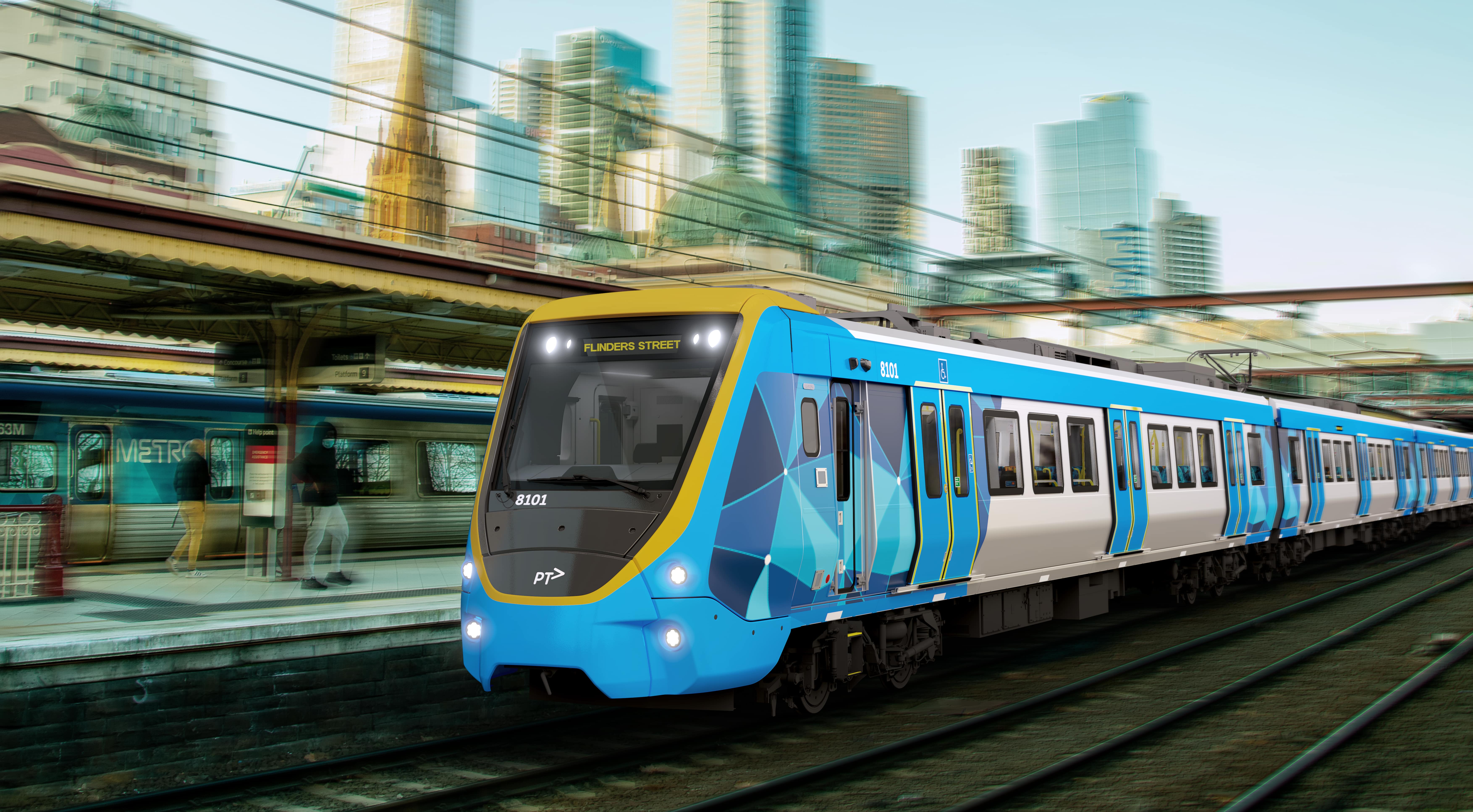 Render of the X'Trapolis 2.0 train arriving at Flinders Street Station. The train, wrapped in blue livery, displays 'FLINDERS STREET' on its destination panel and features trainset number 8101 on its front. The blurred background shows motion with the Melbourne skyline and waiting passengers on the platform.