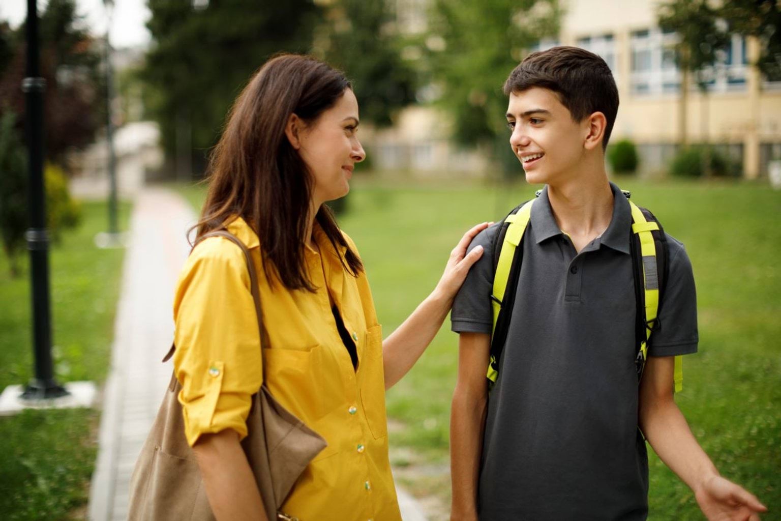 A woman and teenage boy smiley and talking outdoors.