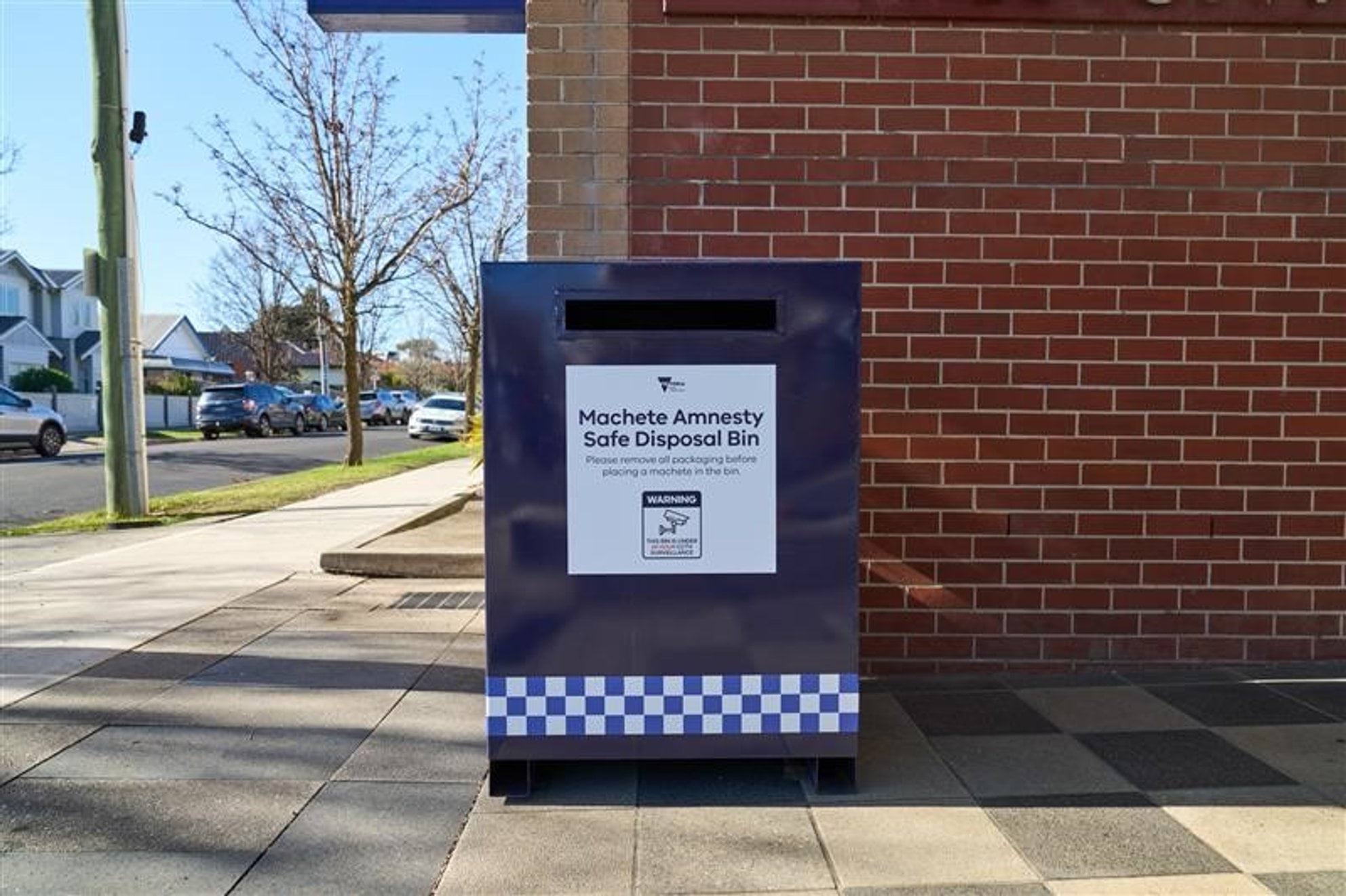 Machete amnesty safe disposal bin in front of a brick building 