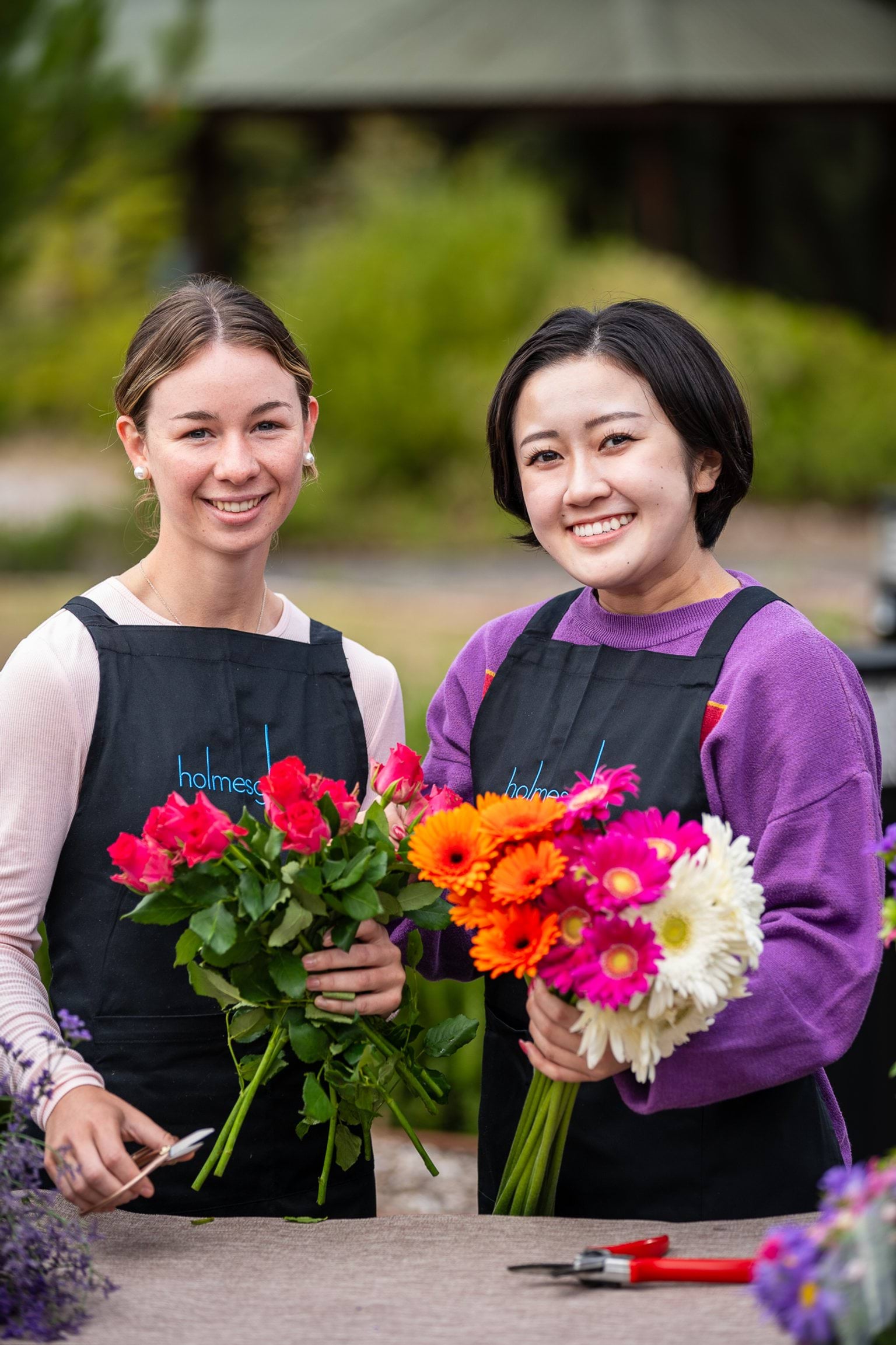 Two people in black aprons holding flowers and smiling.