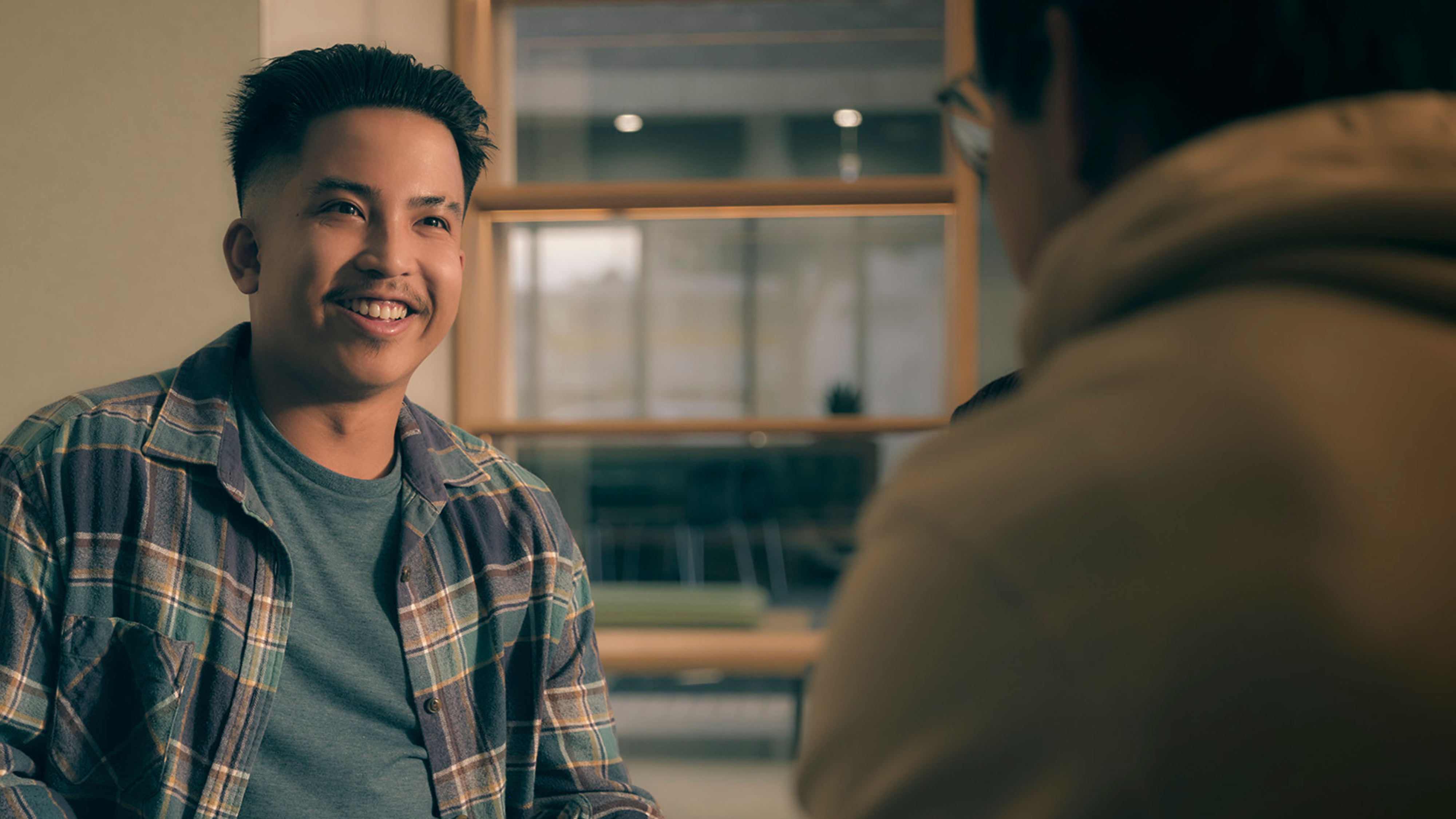 A person smiling and talking to someone with their back to the camera.