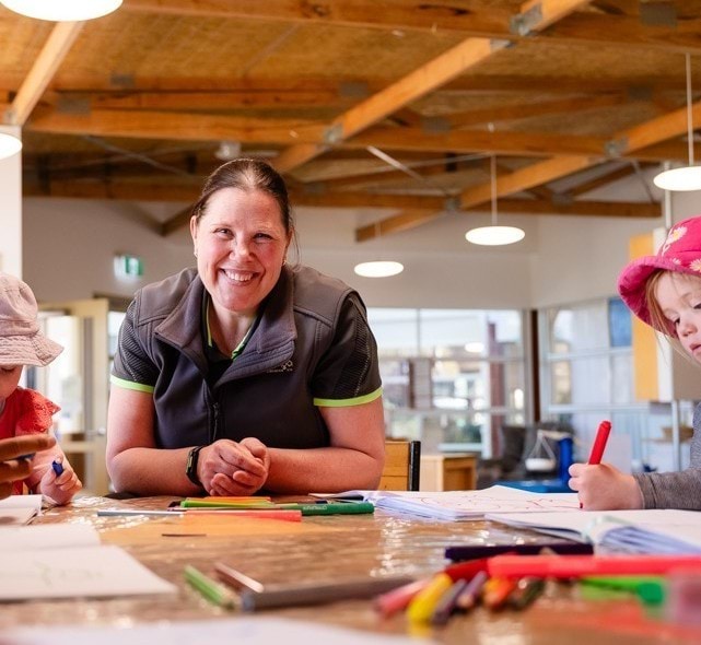 Megan Hancock sitting at a table with 2 children who are drawing.