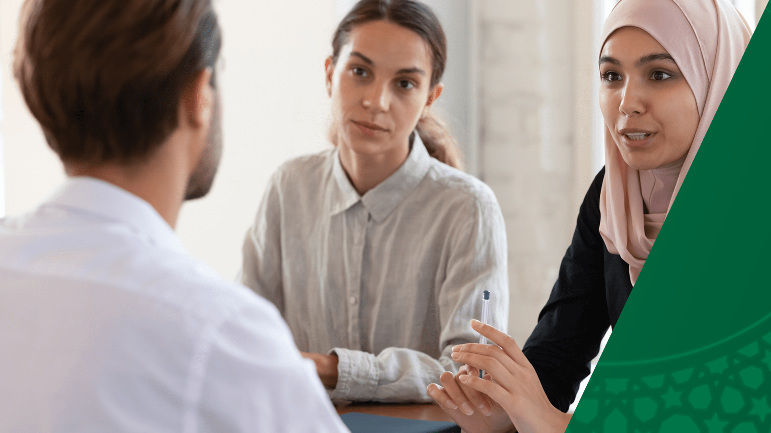 A women in a hijab is seated at a table speaking to a man across the table