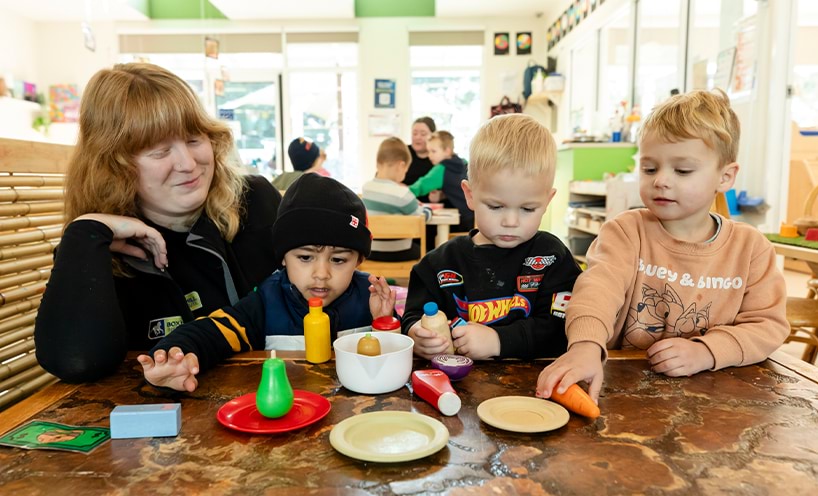 A teacher and 3 small children playing with toys at a table.