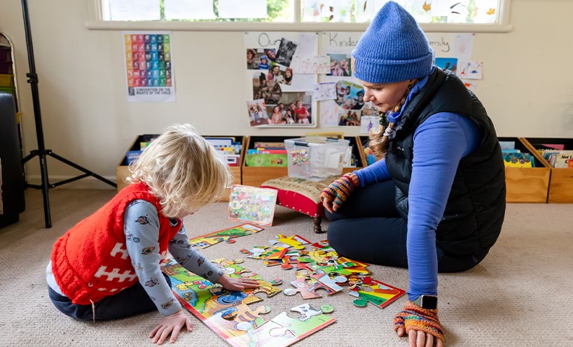 Teacher and child sitting on the floor doing a jigsaw puzzle.
