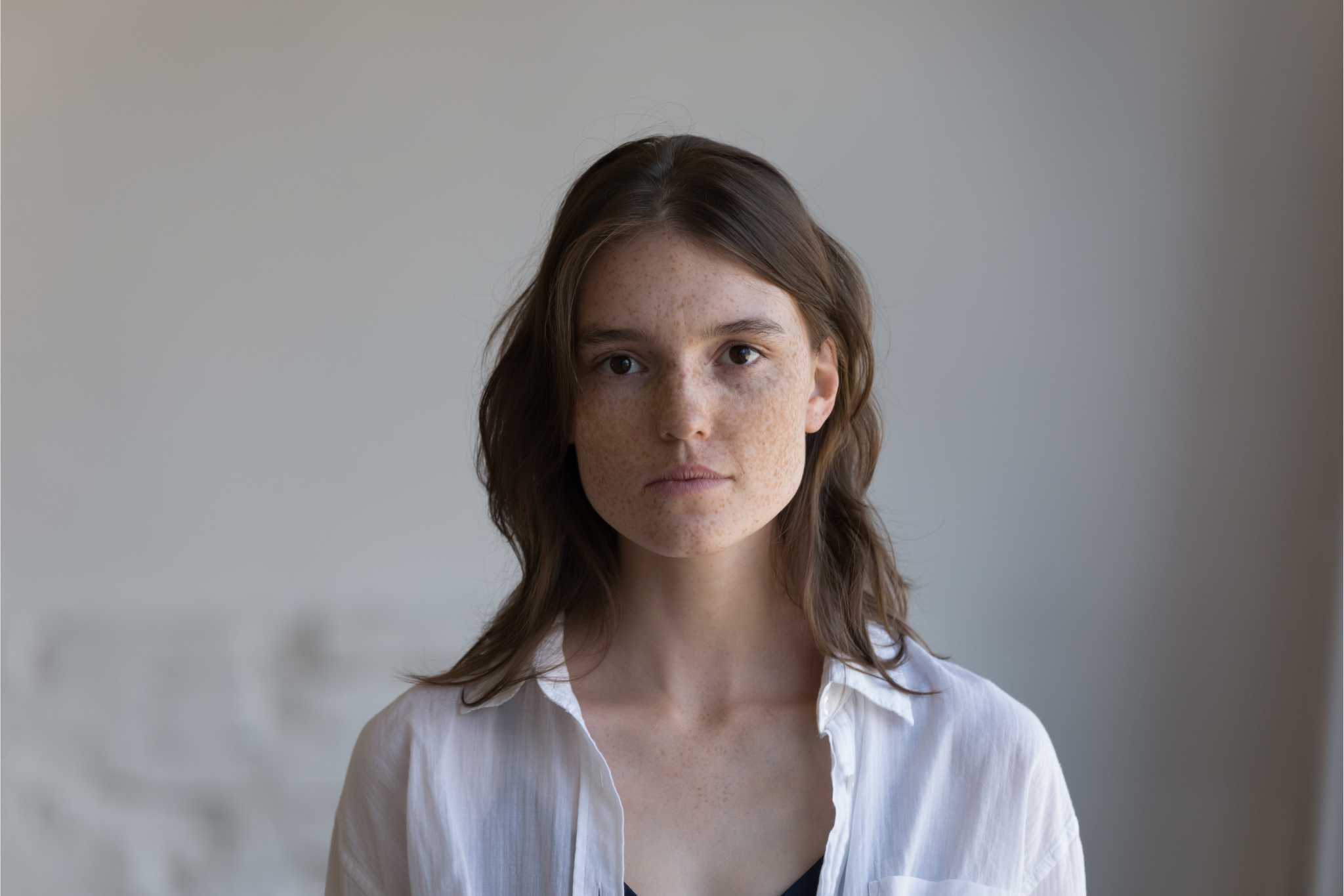 A woman looks directly into the camera with a neutral expression