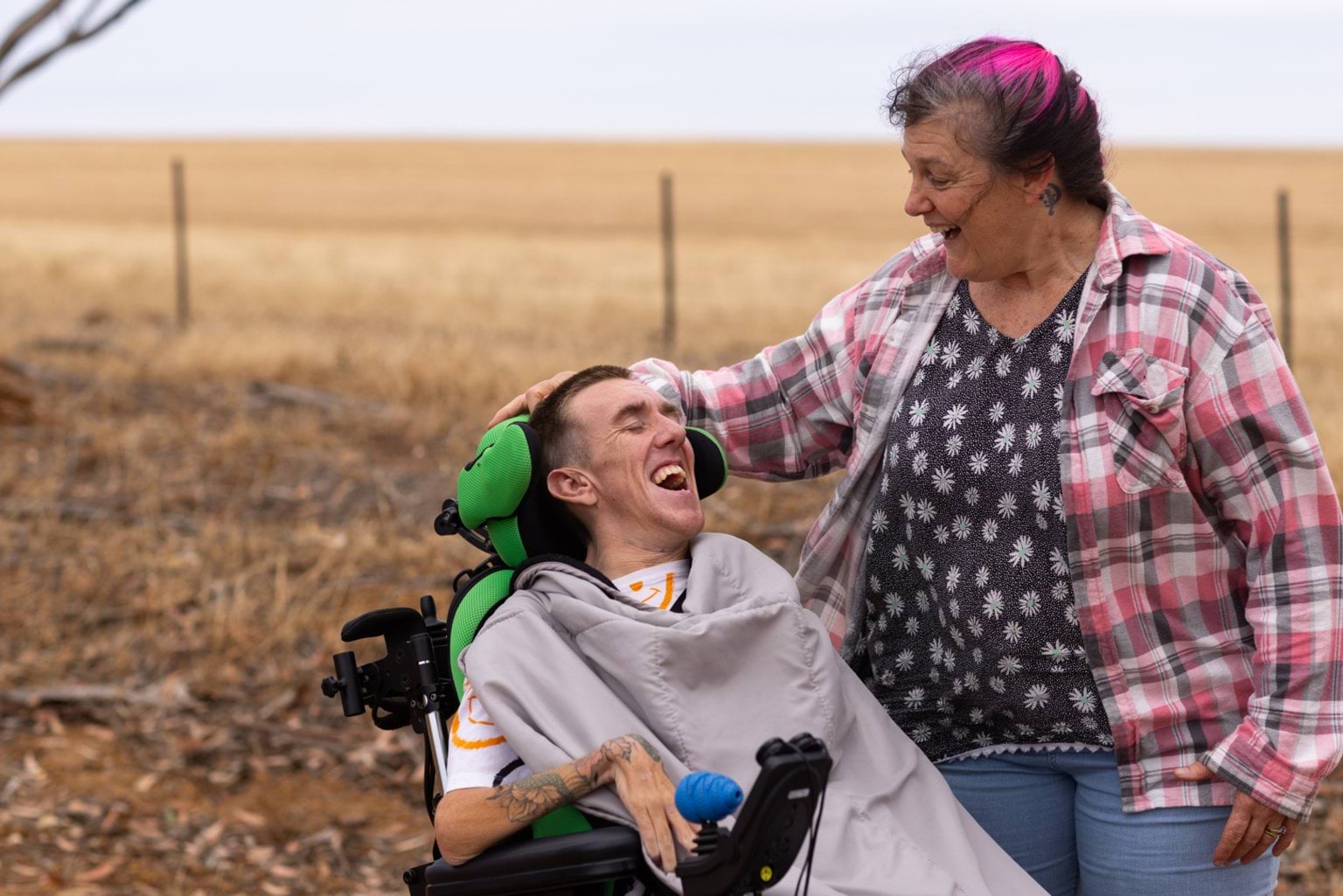 Young man with disability laughing with mother on dirt road in rural Australia