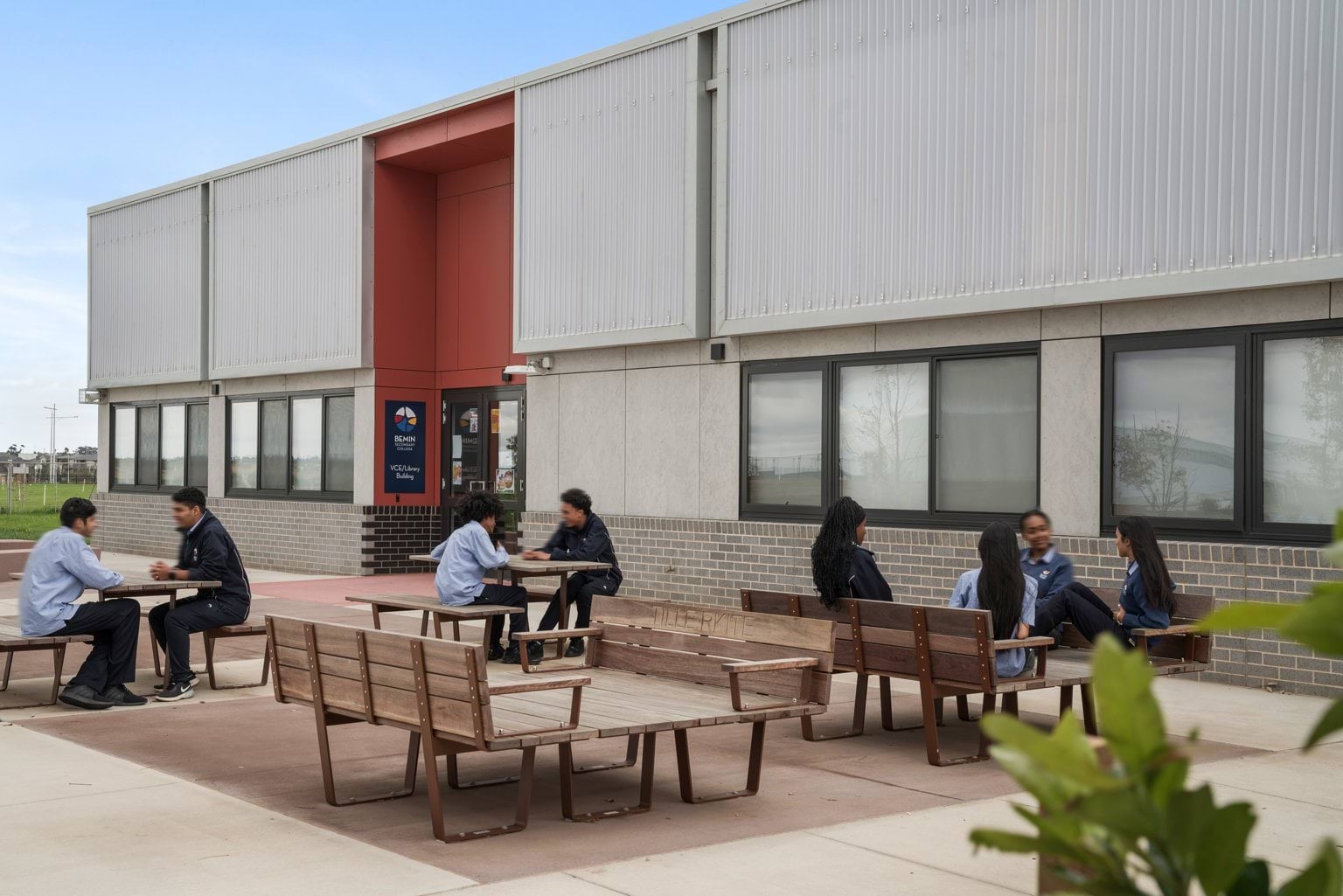 High school ages students sitting at tables in front of a grey building