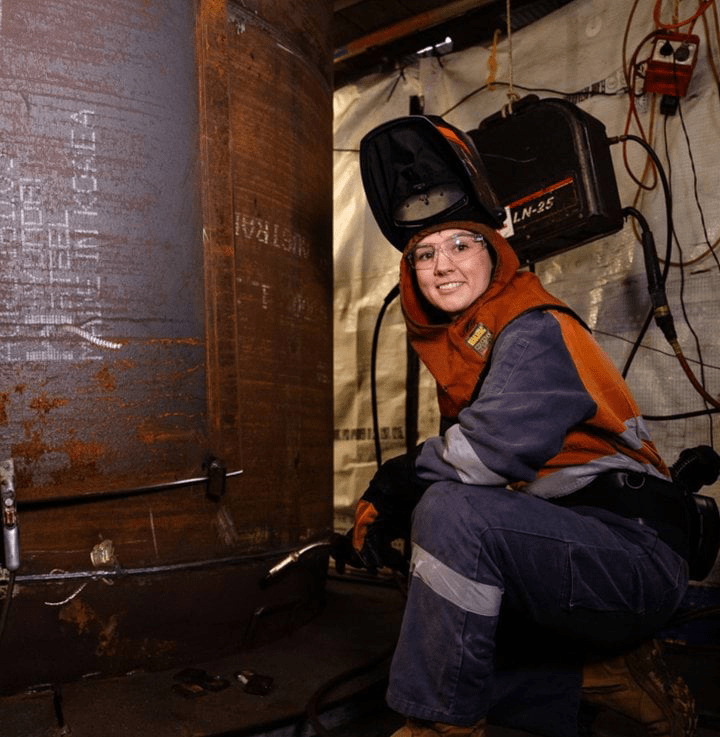 Amber in her workplace holding welding equipment and wearing PPE