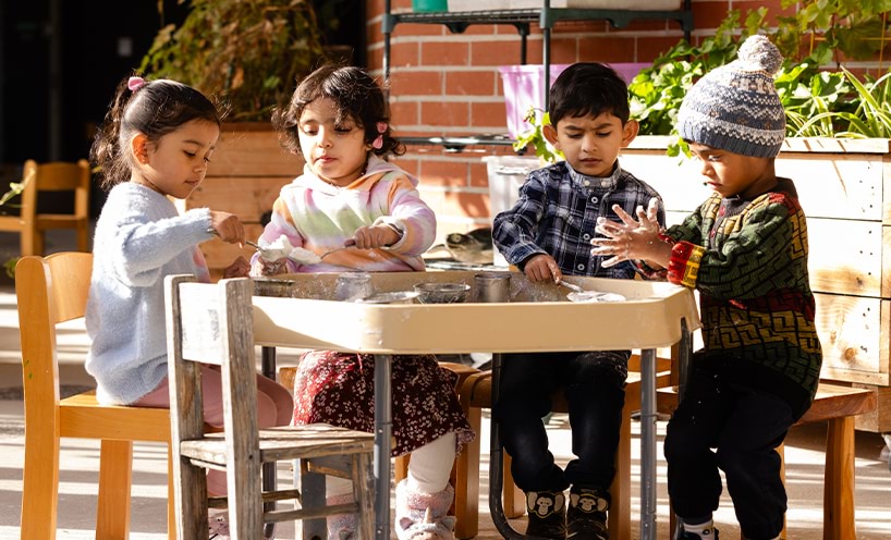 4 children sitting around and playing at the sensory table