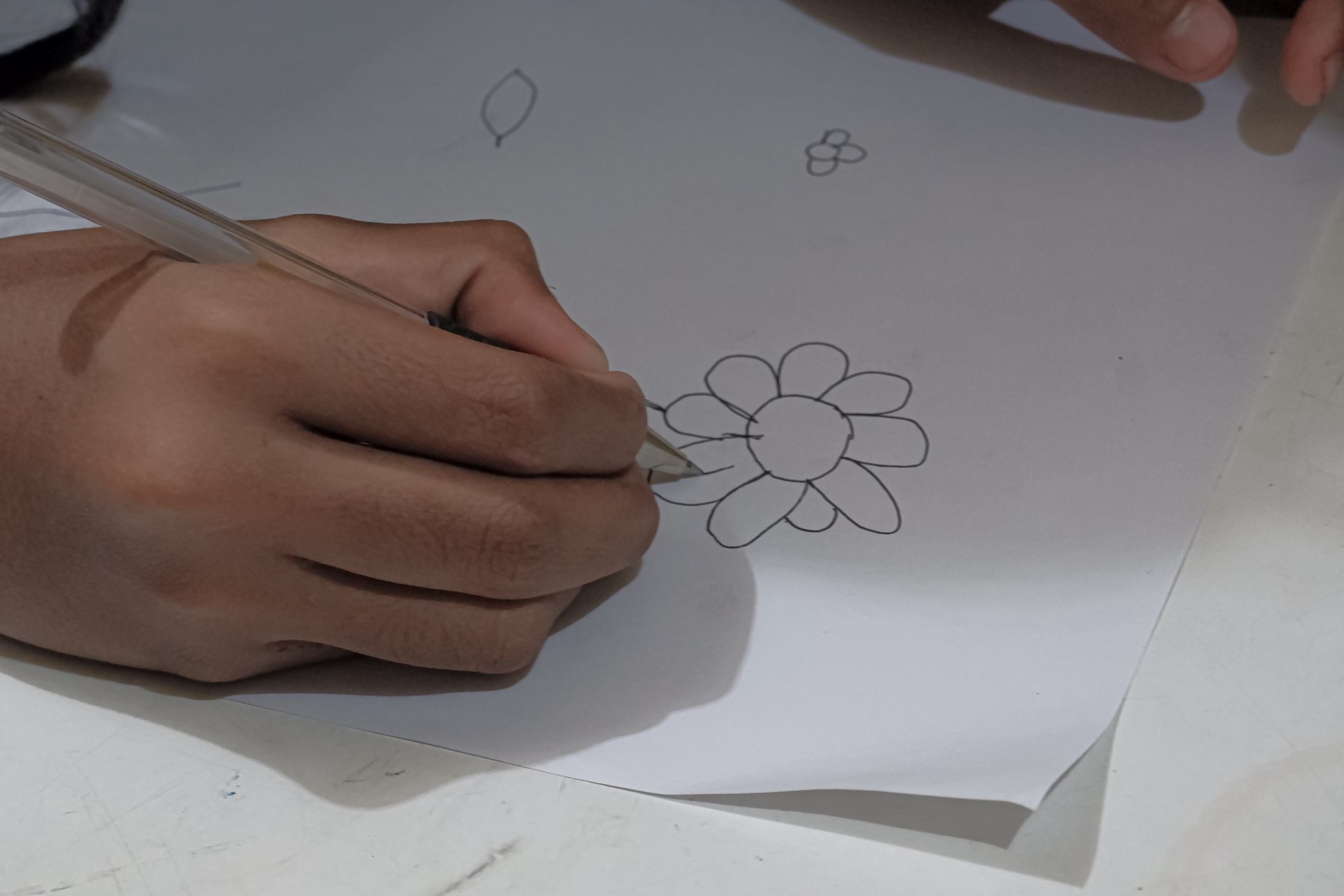 A hand holding a pen and drawing a flower on paper.