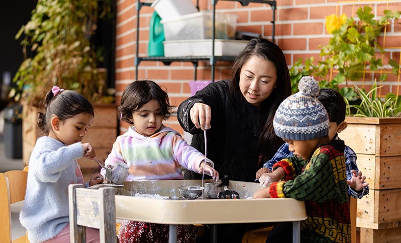 An educator assisting a group of children around a sensory table