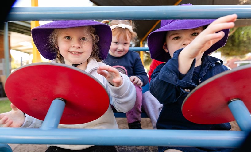 3 children sitting on a toy car with the two of them sat on the front seats with steering wheels